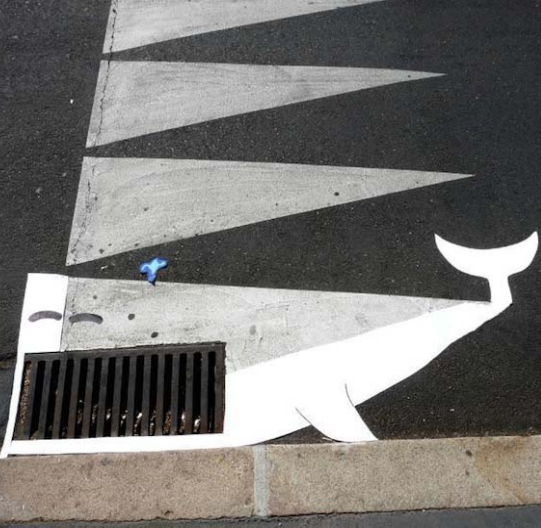 Illustration représentant une oeuvre de l'artiste Oakoak : une baleine peinte au sol, dont la bouche est une grille d'égout.